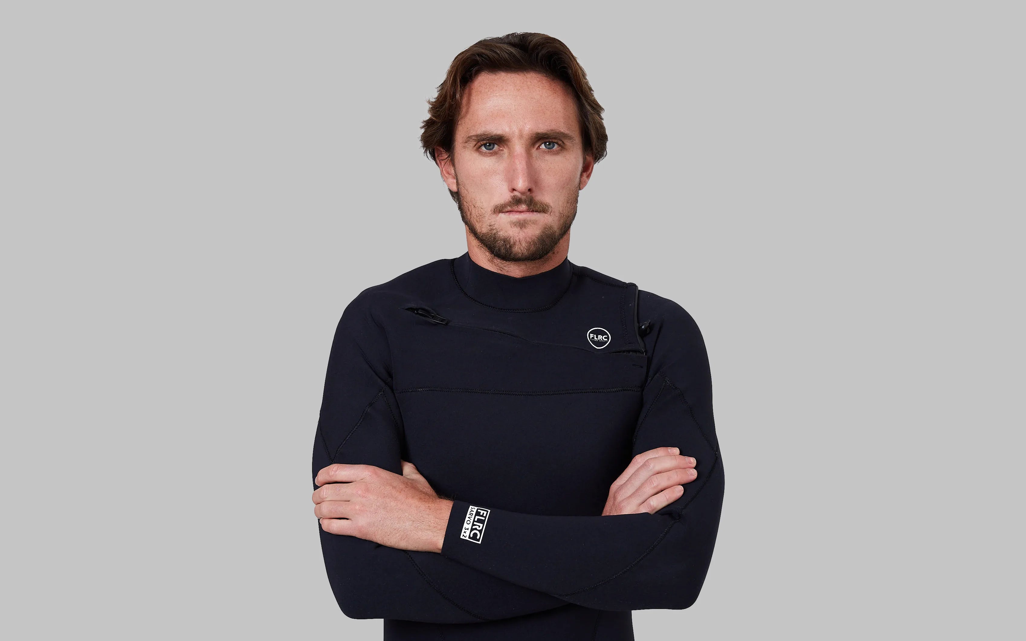 Man wearing Flatrock FLRC Sarvo Series 2 men's chest-zip steamer wetsuit with arms crossed showcasing premium fit and construction for surfing